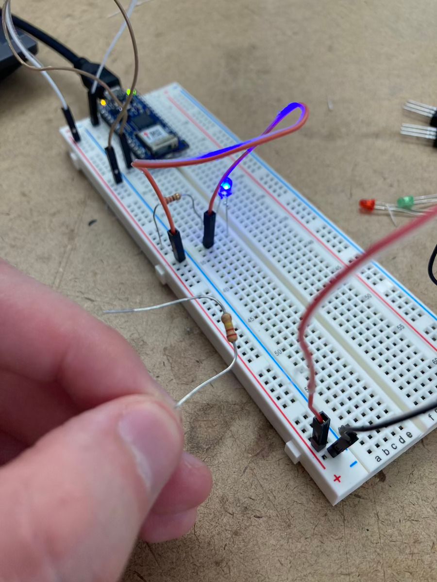 A breadboard with one lit LED. I'm holding a 220KΩ resistor is held next to the breadboard.