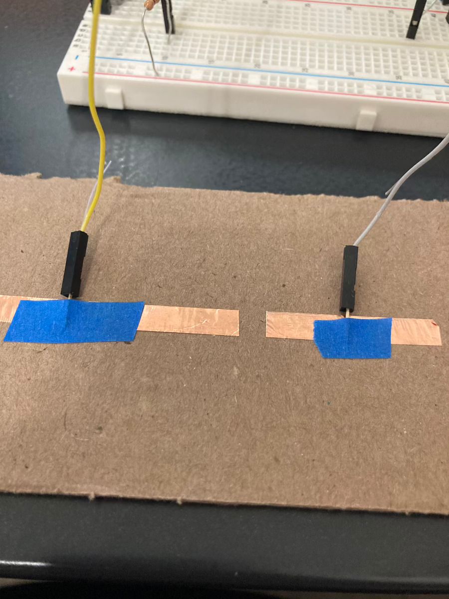 Two pieces of conductive tape on a piece of cardboard, with wires taped to each.